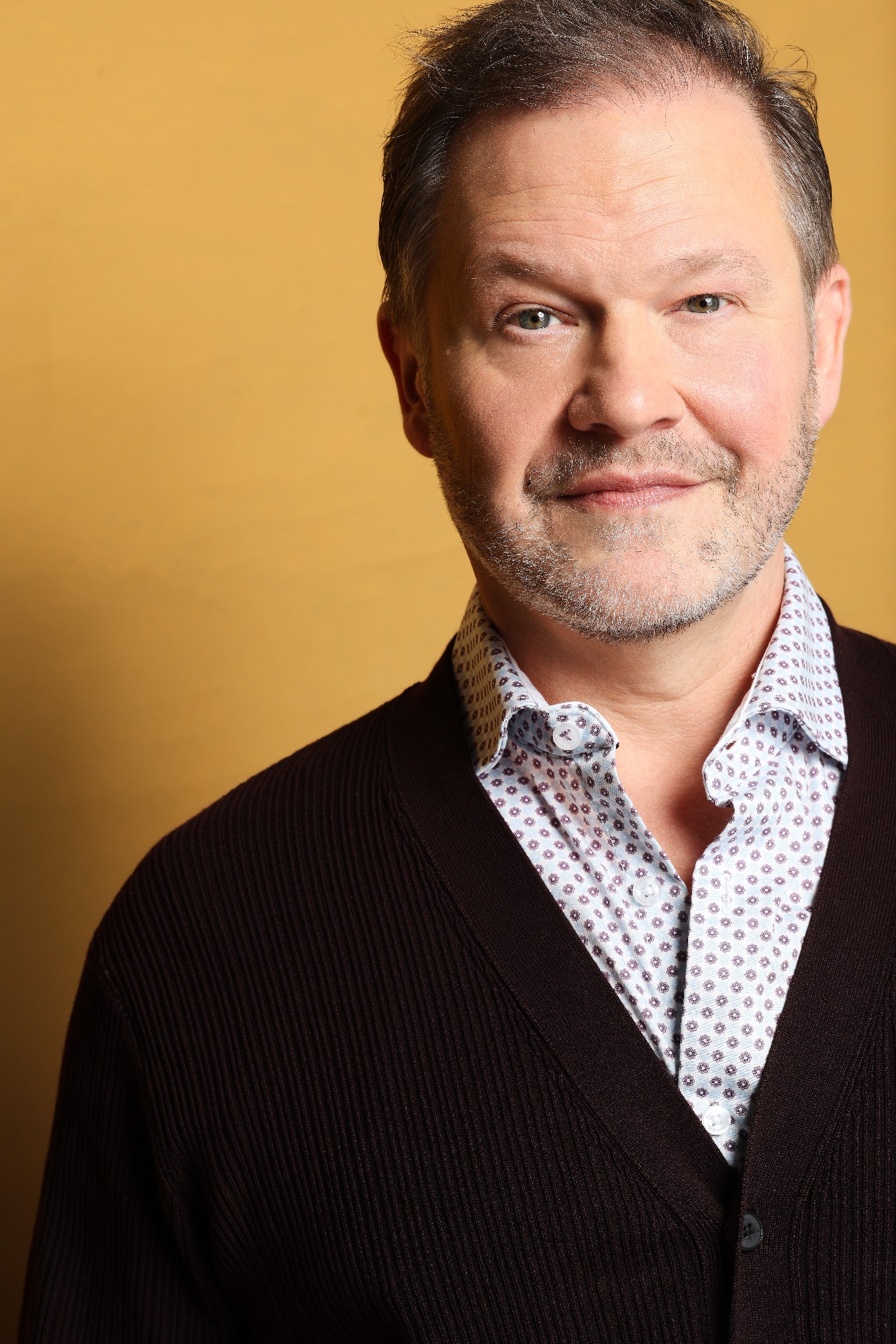Harry Clark in a dark cardigan against a warm gold background